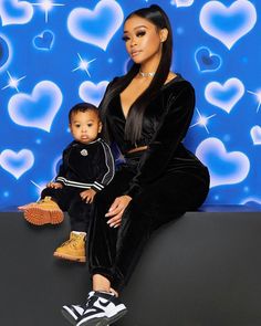 a woman sitting on top of a black couch next to a baby in front of a blue background