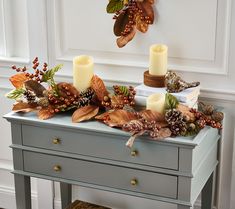 a table with candles, leaves and other decorations on it in front of a white wall