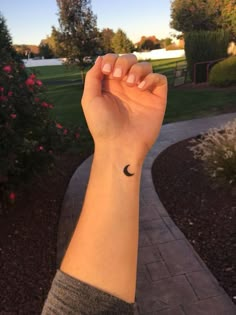 a woman's arm with a small black crescent tattoo on the left side of her wrist