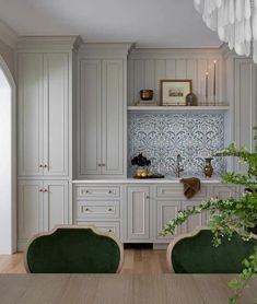 a kitchen with white cabinets and green chairs in front of a wooden table surrounded by potted plants