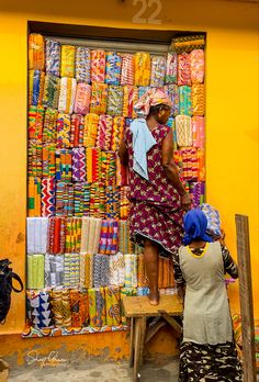 two women standing in front of a store selling colorful fabrics