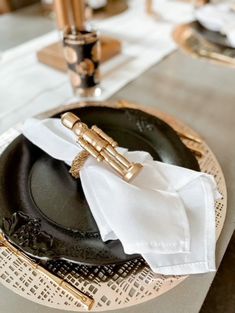 a black plate topped with a white napkin next to a gold and silver place setting