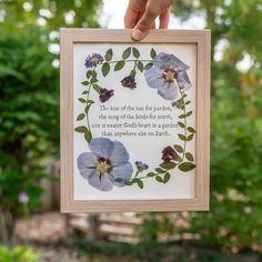 a person holding up a framed art piece with flowers in the middle and a quote on it