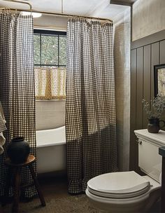 a white toilet sitting next to a bath tub in a bathroom under a window with curtains