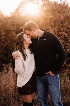 a man and woman kissing in front of some tall grass with the sun behind them