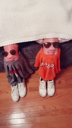 two small dolls are under a bed with sunglasses on their heads and one is wearing an orange shirt