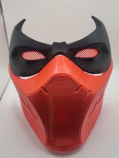 an orange and black mask with red eyes on it's face is sitting on a white surface