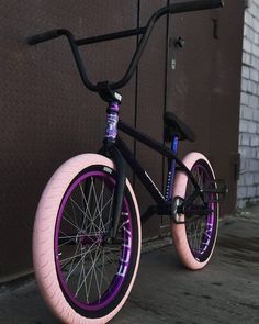 a black and purple bike parked next to a building with pink rims on it