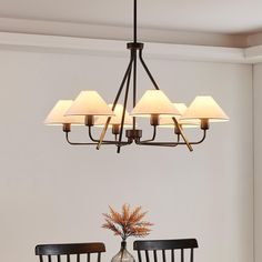 a chandelier hanging over a dining room table with four chairs and a vase filled with flowers