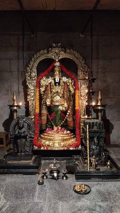 the statue is surrounded by candles and other items in front of it, including an idol