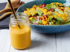 a blue bowl filled with salad next to a jar of dressing