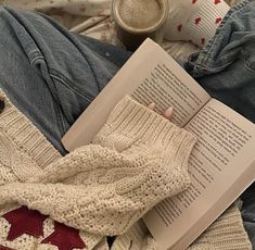 an open book on top of a bed next to a pair of jeans and mittens