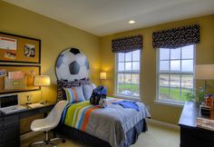 a bedroom with a soccer ball on the bed and desk in front of two windows