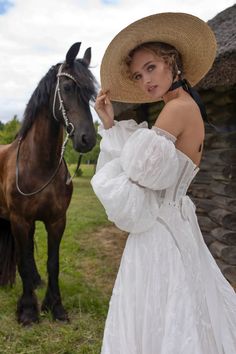 a woman in a white dress standing next to a brown horse wearing a straw hat