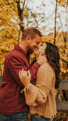 a man and woman standing next to each other in front of trees with yellow leaves