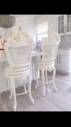 two white chairs sitting at a table in a kitchen next to an island with flowers on it