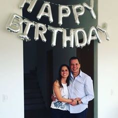 a man and woman are standing in front of a happy birthday sign with the words happy birthday on it