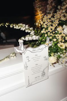 a wedding card sitting on top of a window sill with flowers in the background