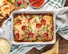 a casserole dish with tomatoes, cheese and sauces on a wooden table