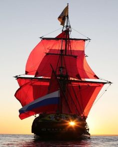 a large red sail boat sailing across the ocean at sunset or sunrise with its sails down