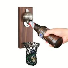 a person is holding a beer bottle near a basket and a wall mounted hook on a door