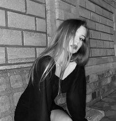 a black and white photo of a woman sitting on a bench in front of a brick wall