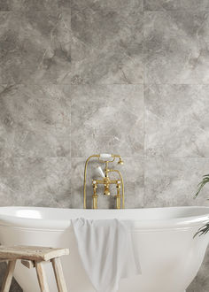 a white bath tub sitting next to a wooden stool in front of a tiled wall