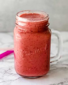 a glass jar filled with red liquid sitting on top of a marble counter next to a pink ribbon