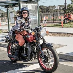 a woman riding on the back of a motorcycle down a street next to a bus stop