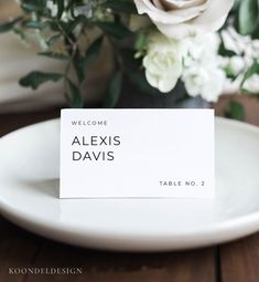 a place card sitting on top of a white plate next to a bouquet of flowers