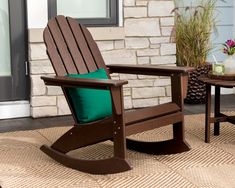 a wooden rocking chair sitting on top of a rug next to a table with a green pillow