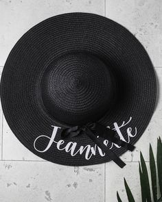 a black hat with the word jeanie written on it next to a potted plant