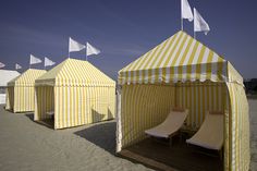 some yellow and white striped tents sitting on the beach with lounge chairs in front of them