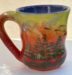 a ceramic mug with an orange and blue handle sits on a white countertop next to a window