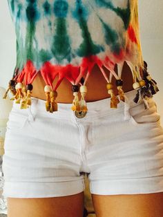 a woman wearing white shorts and a tie dye shirt with tassels on her waist