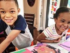 two young children sitting at a table with paper cutouts on it and one child smiling