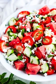 a salad with strawberries, cucumbers and feta cheese on top in a white bowl