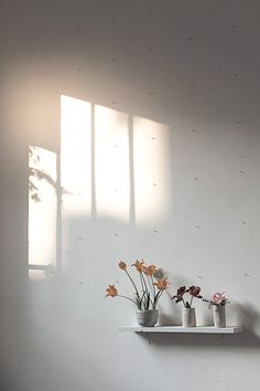 three white vases with flowers in them on a shelf next to a window sill