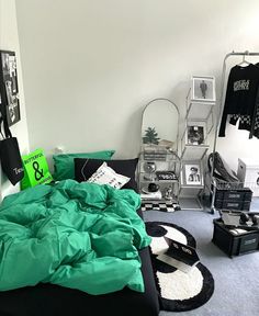 an unmade bed with green sheets and pillows in a white room filled with pictures