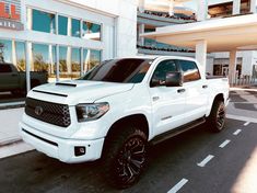 a white truck is parked in front of a building with black wheels and rims