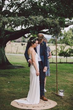 a bride and groom standing in front of a tree at their outdoor wedding ceremony on the grass