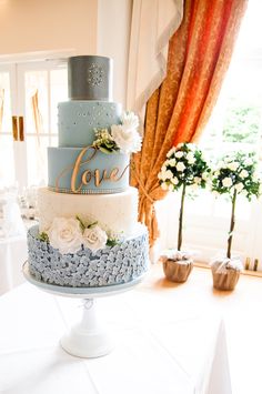 a blue and white wedding cake sitting on top of a table in front of a window