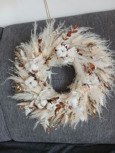 a wreath made out of feathers and cotton on top of a gray couch next to a white wall