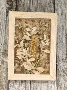 a wooden frame with dried flowers and leaves in it on a wood table next to a wall