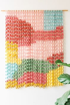 a wall hanging made out of plastic beads with a plant in the corner next to it