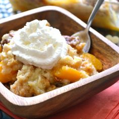 a wooden bowl filled with fruit and topped with whipped cream next to another dish in the background