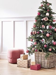 a christmas tree with presents under it in a living room next to a pink ottoman