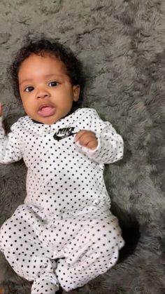 a baby laying on top of a gray carpet wearing a white and black polka dot outfit