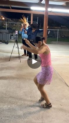 a woman in a pink dress is dancing with other people behind her and one person holding a camera