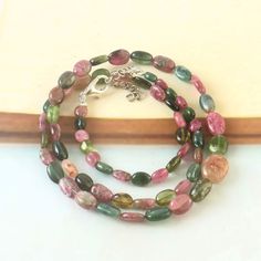 a multi - colored beaded necklace is displayed on a white surface with a wooden bar